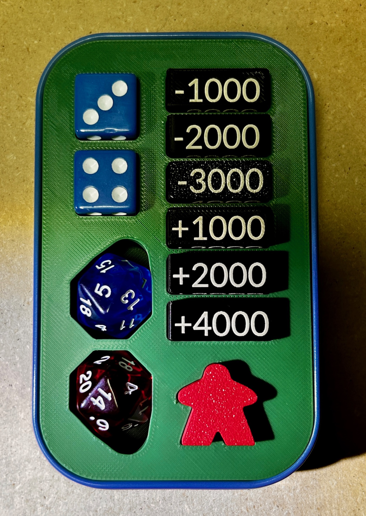 Green 3D-printed TinForge insert fitted inside a blue-rimmed One Piece tin with dice, damage counters, and a red meeple