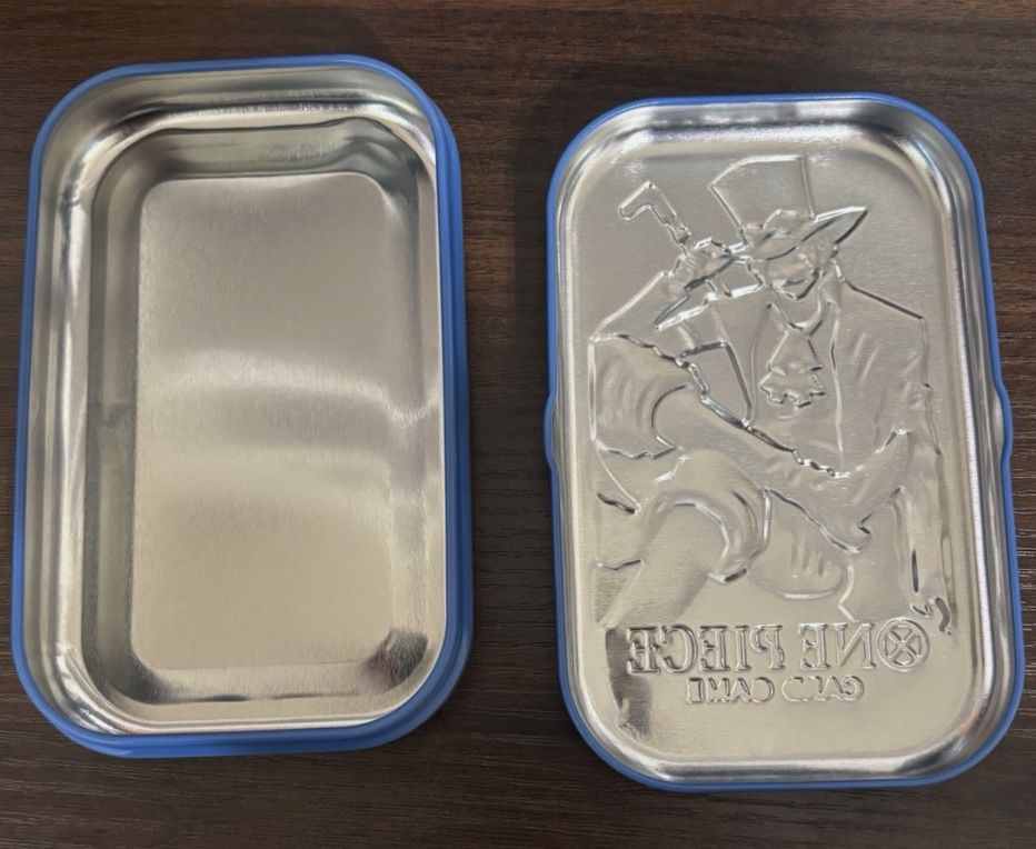An open blue-rimmed One Piece metal tin showing its empty interior and embossed lid